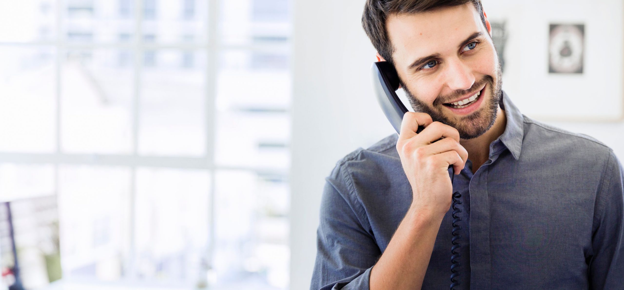 Man in a button up shirt using a corded phone