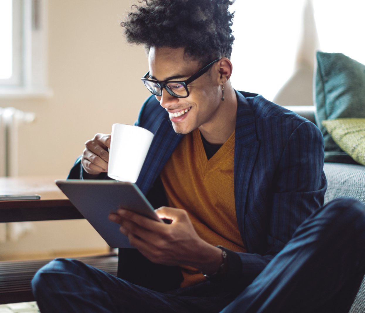 Man in glasses drinking coffee while browsing the internet on a tablet