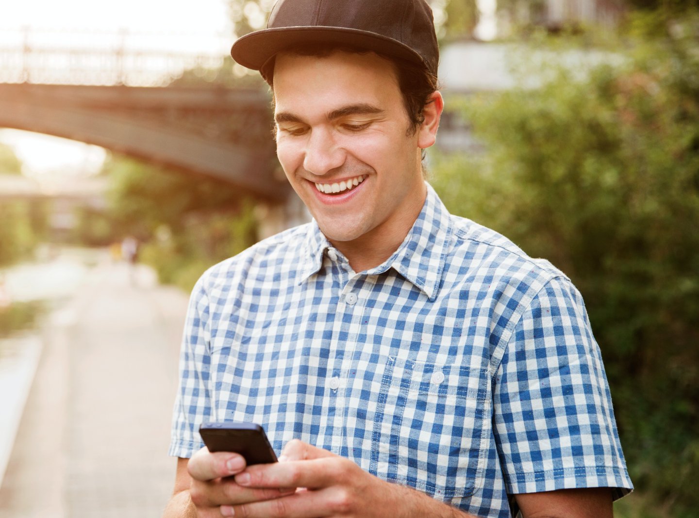 Man in a hat happily using his phone outside