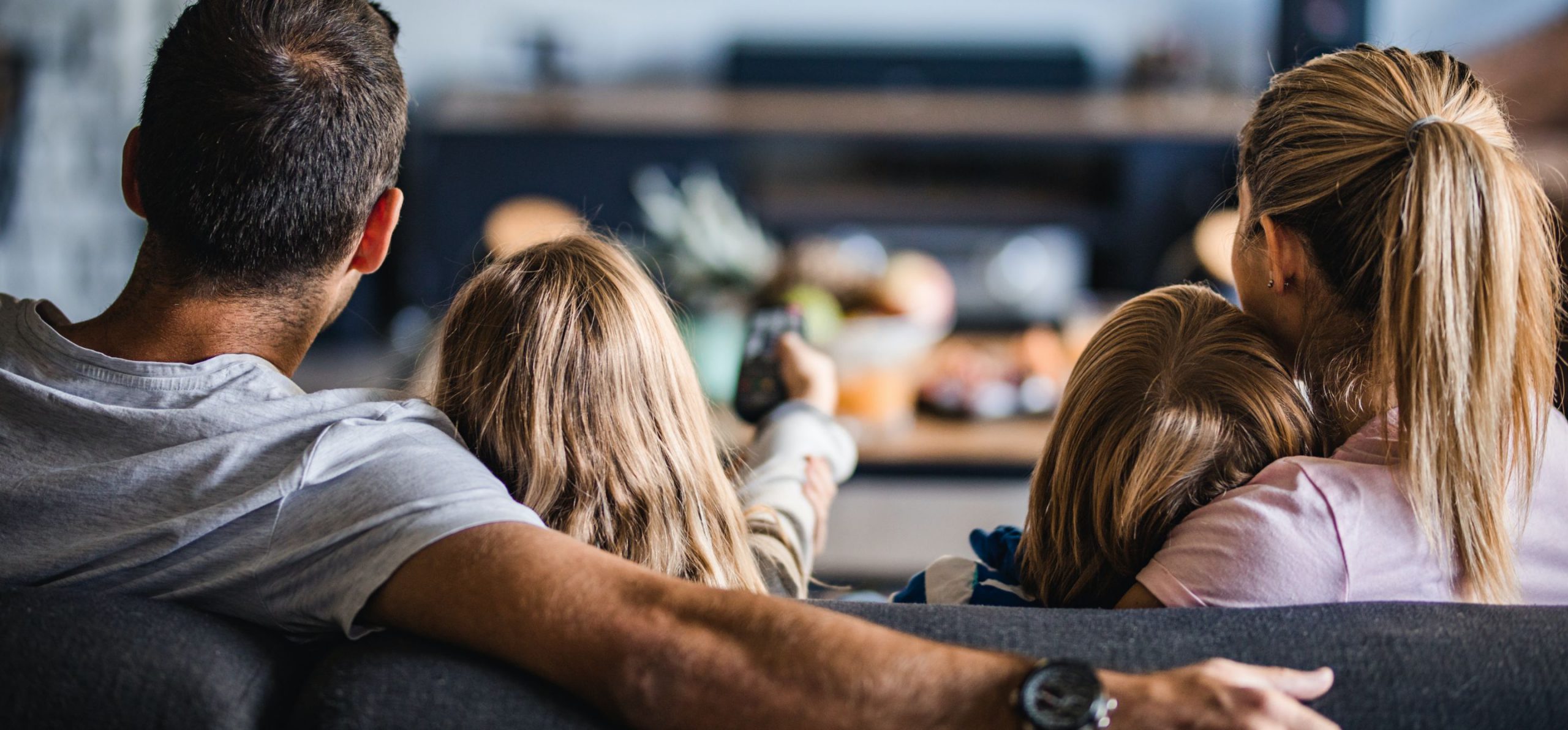 Family sitting on a couch watching tv and changing channels