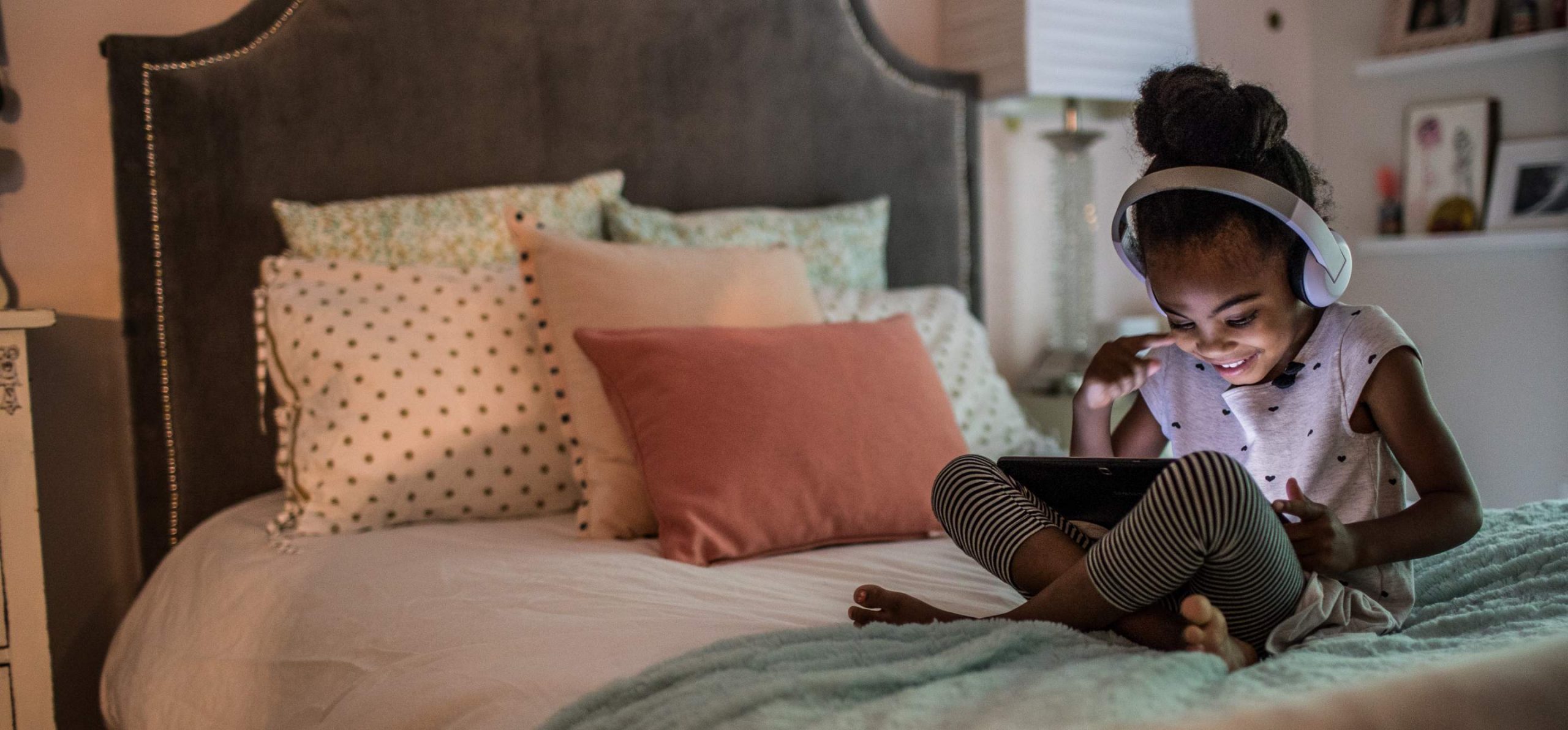 Young girl sitting on her bed at night watching a video on a tablet