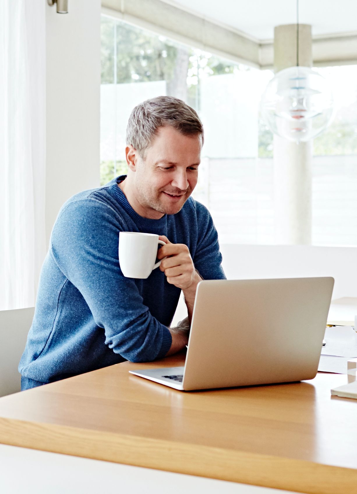 Man in home looking at laptop while drinking coffee